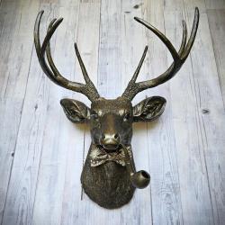 faux taxidermy deer head wall mount, painted rubbed bronze and accented in antique gold. a pipe extends from the deers mouth and a monocle on a chain is also the deers head along with a fabric bow tie