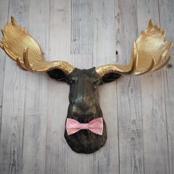 Faux taxidermy moose head, head is painted black with gold accents, antlers painted metallic gold, a pink quatrefoil bow tie accents the neck of the moose.