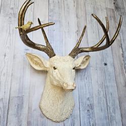 Faux taxidermy deer head, painted antique white with antique gold accenting. The antlers are antique gold a small brass bird is perched on the left facing antler.