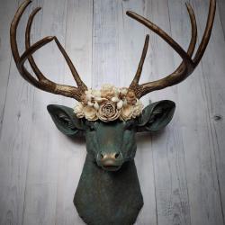 Faux taxidermy deer head painted verdigris with antique gold antlers. A floral crown made of cream sola flowers rests atop the deers head.