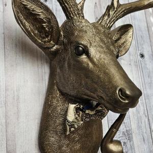 Faux taxidermy deer head with smoking pipe and bow tie, painted antique gold with dark bronze accents.