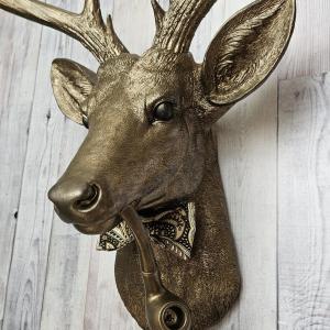 Faux taxidermy deer head with smoking pipe and bow tie, painted antique gold with dark bronze accents.