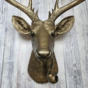 Faux taxidermy deer head wall mount with smoking pipe, painted antique gold with dark bronze accenting.
