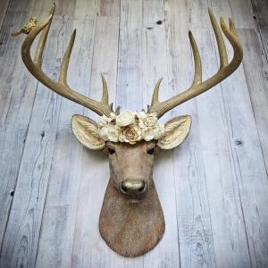 Faux taxidermy deer head, painted in natural colors with a brass bird on one antler and a wooden flower crown atop it's head.