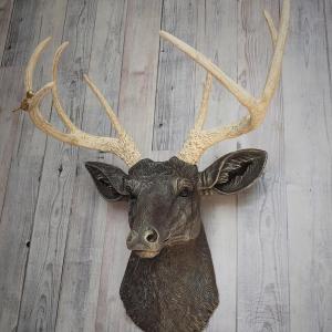 Faux taxidermy deer head painted chestnut brown with cream and gold accenting. Cream antlers with gold antlers, a brass bird rests atop one of the antlers.