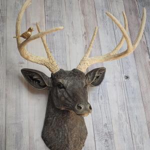 Faux taxidermy deer head painted chestnut brown with cream and gold accenting. Cream antlers with gold antlers, a brass bird rests atop one of the antlers.