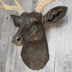 Faux taxidermy deer head painted chestnut brown with cream and gold accenting. Cream antlers with gold antlers, a brass bird rests atop one of the antlers.