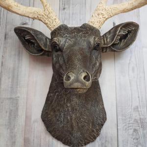 Faux taxidermy deer head painted chestnut brown with cream and gold accenting. Cream antlers with gold antlers, a brass bird rests atop one of the antlers.