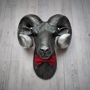 Faux taxidermy ram head wall mount, painted black with metallic silver tipped horns with graduating silver going to the head. A red and black polka dot bow tie accents the neck of the ram.