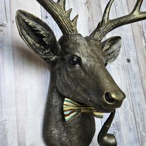faux taxidermy deer head, rubbed bronze with gold accents. A smoking pipe hangs from the deers mouth and its wearing a striped bow tie