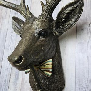 faux taxidermy deer head, rubbed bronze with gold accents. A smoking pipe hangs from the deers mouth and its wearing a striped bow tie