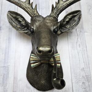 faux taxidermy deer head, rubbed bronze with gold accents. A smoking pipe hangs from the deers mouth and its wearing a striped bow tie