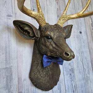 Faux taxidermy deer head painted chestnut brown with gold antlers. A blue bow tie accents the deers neck.