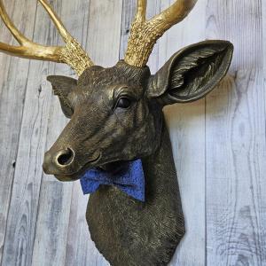 Faux taxidermy deer head painted chestnut brown with gold antlers. A blue bow tie accents the deers neck.