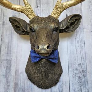 Faux taxidermy deer head painted chestnut brown with gold antlers. A blue bow tie accents the deers neck.