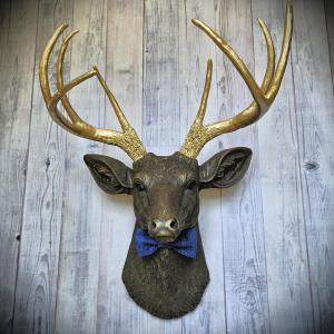 Faux taxidermy deer head painted chestnut brown with gold antlers. A blue bow tie accents the deers neck.
