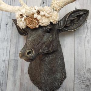 Faux taxidermy deer head, painted chestnut brown with antique white and gold accenting. Antlers are antique white with gold and chestnut brown accenting. A cream floral crown rests atop the deers head.