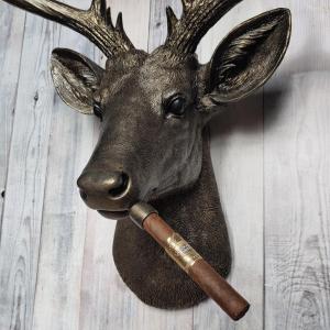 Faux taxidermy deer head painted rubbed bronze with rubbed bronze antlers and gold accents. A cigar is in the deers mouth.