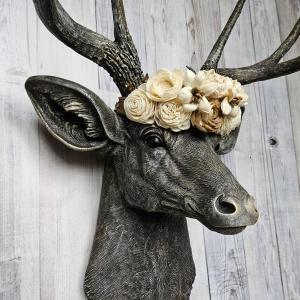 faux taxidermy deer head, painted chestnut brown with gold and antique white accents. The antlers have been painted in the same color combination. A floral crown made of cream and natural bark sola flowers rests atop the deers head.