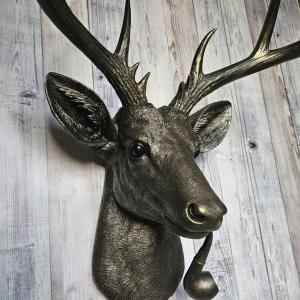 Rubbed bronze faux taxidermy deer head with gold accents. A smoking pipe extends from the deers mouth