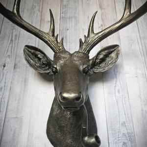 Rubbed bronze faux taxidermy deer head with gold accents. A smoking pipe extends from the deers mouth