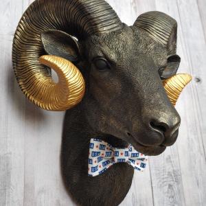 Faux taxidermy ram head wall mount, painted black with metallic gold tipped horns with graduating gold going to the head. A USA bow tie accents the neck of the ram.