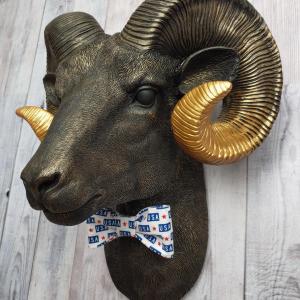 Faux taxidermy ram head wall mount, painted black with metallic gold tipped horns with graduating gold going to the head. A USA bow tie accents the neck of the ram.