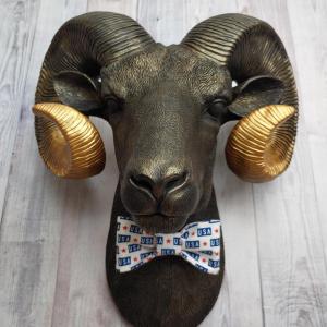 Faux taxidermy ram head wall mount, painted black with metallic gold tipped horns with graduating gold going to the head. A USA bow tie accents the neck of the ram.