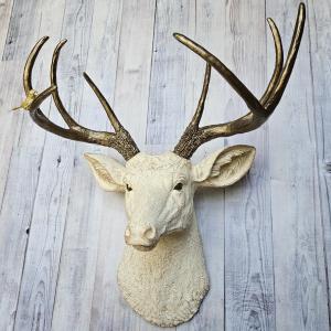 Faux taxidermy deer head, painted antique white with antique gold accenting. The antlers are antique gold a small brass bird is perched on the left facing antler.