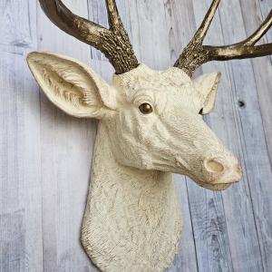 Faux taxidermy deer head, painted antique white with antique gold accenting. The antlers are antique gold a small brass bird is perched on the left facing antler.
