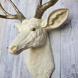 Faux taxidermy deer head, painted antique white with antique gold accenting. The antlers are antique gold a small brass bird is perched on the left facing antler.