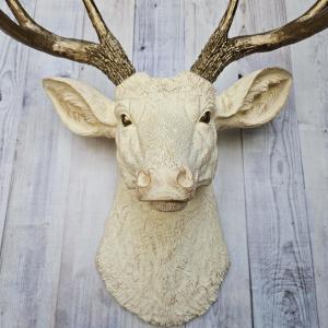 Faux taxidermy deer head, painted antique white with antique gold accenting. The antlers are antique gold a small brass bird is perched on the left facing antler.