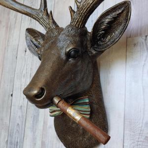 Faux taxidermy deer head painted rubbed bronze with rubbed bronze antlers and gold accents. A cigar is in the deers mouth and a bow tie accents the deers neck.