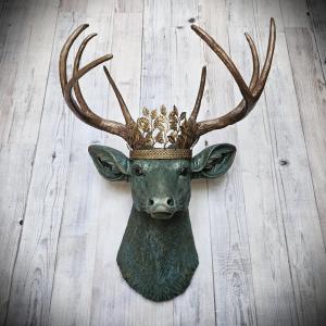Faux taxidermy deer head wall mount, head is painted verdigris with antique gold antlers. A metal leaf crown rests atop the deers head.