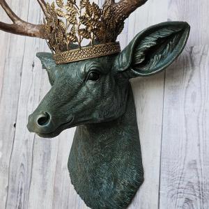 Faux taxidermy deer head wall mount, head is painted verdigris with antique gold antlers. A metal leaf crown rests atop the deers head