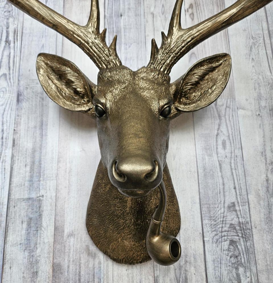 Faux taxidermy deer head wall mount with smoking pipe, painted antique gold with dark bronze accenting.
