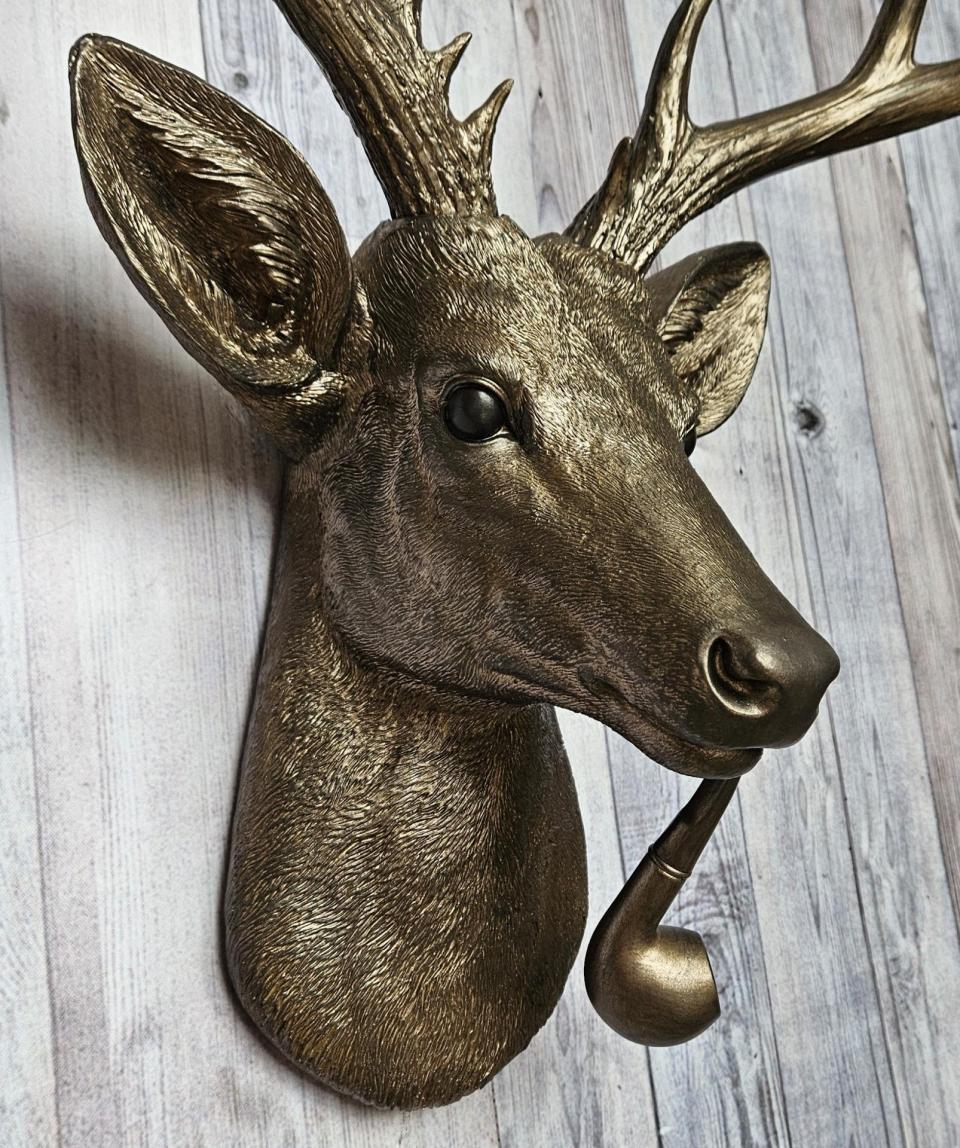 Faux taxidermy deer head wall mount with smoking pipe, painted antique gold with dark bronze accenting.