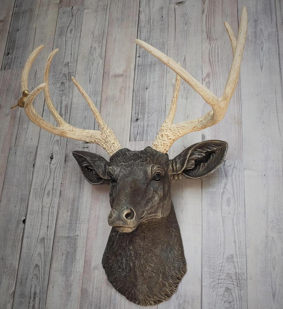 Faux taxidermy deer head painted chestnut brown with cream and gold accenting. Cream antlers with gold antlers, a brass bird rests atop one of the antlers.