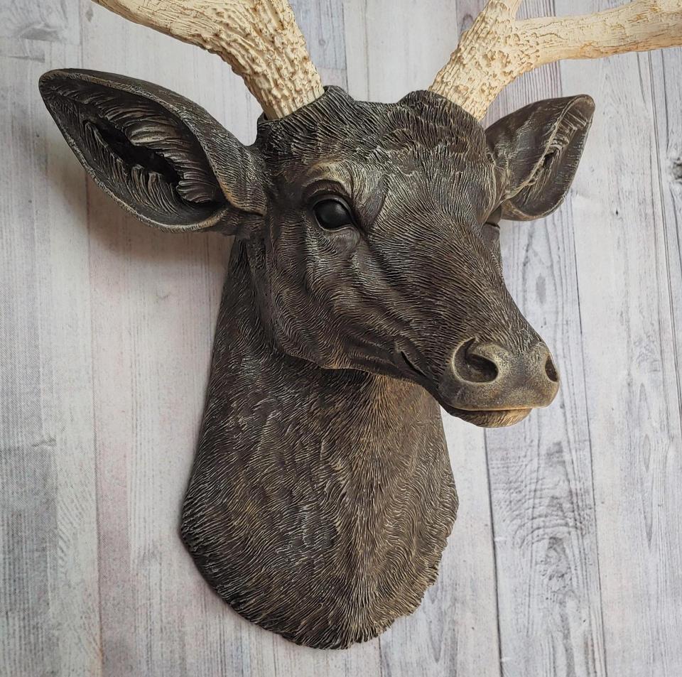 Faux taxidermy deer head painted chestnut brown with cream and gold accenting. Cream antlers with gold antlers, a brass bird rests atop one of the antlers.