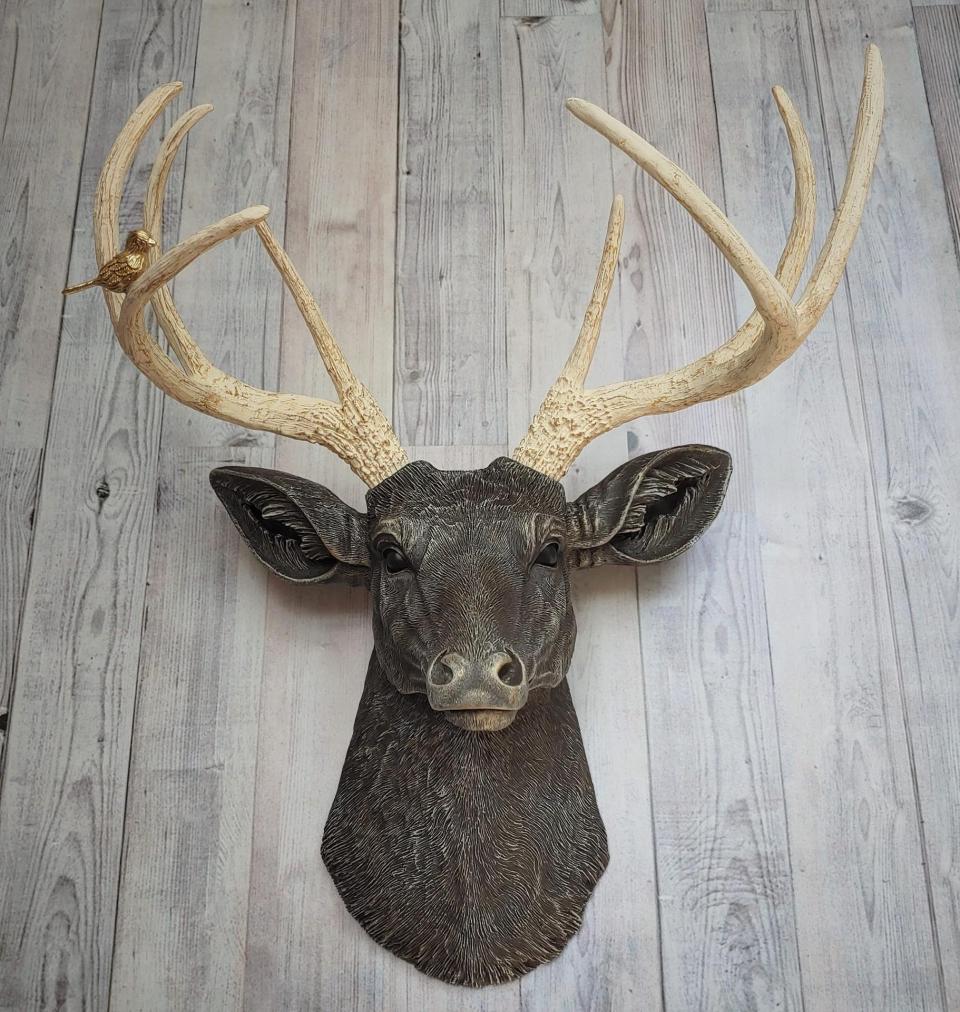 Faux taxidermy deer head painted chestnut brown with cream and gold accenting. Cream antlers with gold antlers, a brass bird rests atop one of the antlers.