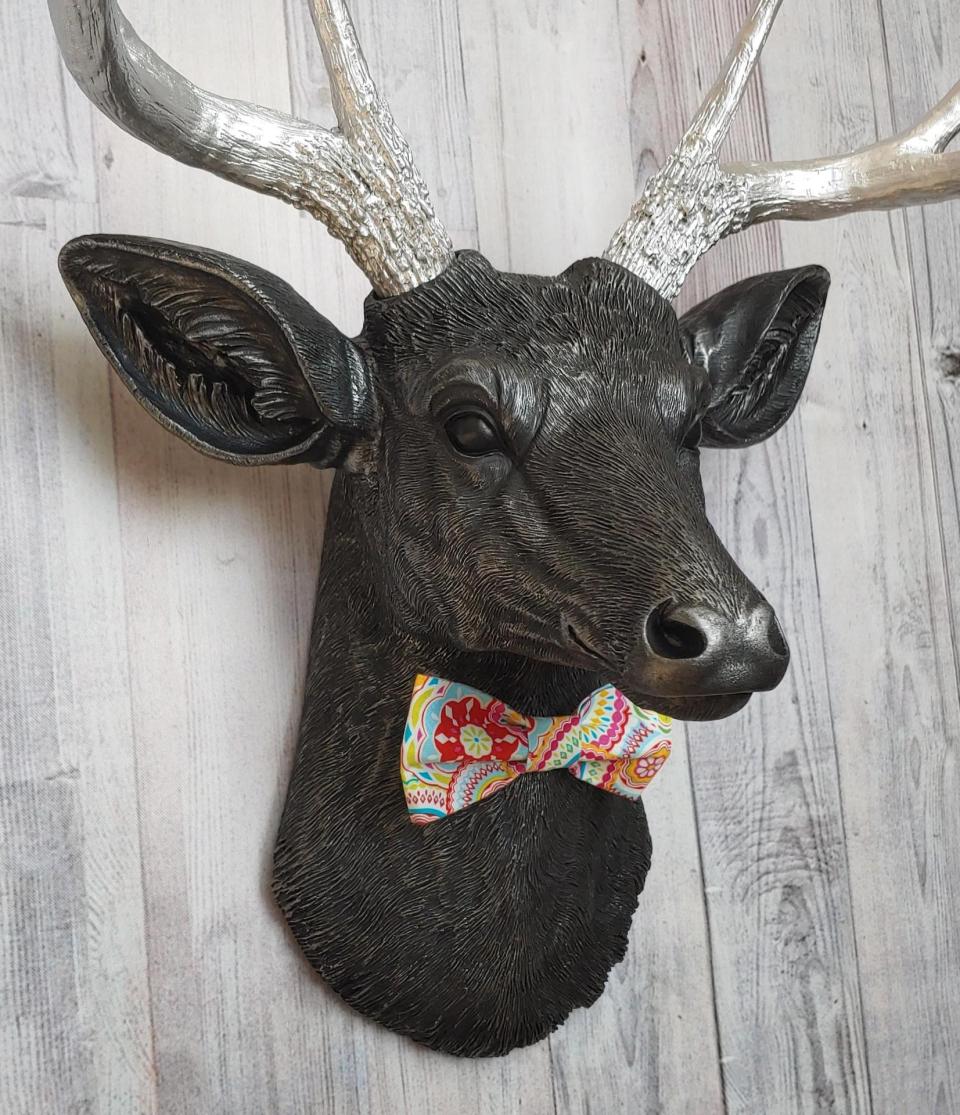Faux taxidermy deer head painted black with silver antlers and a removable bright multi colored bow tie