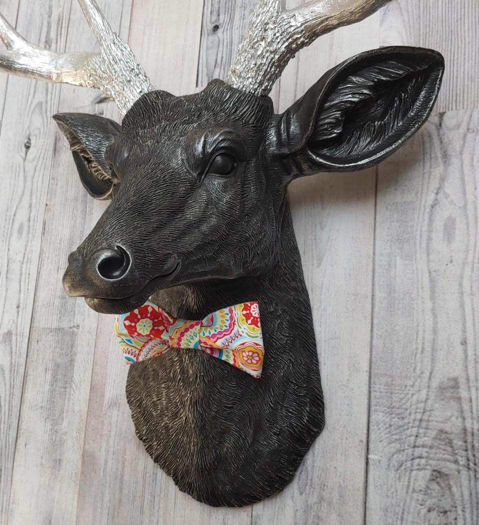 Faux taxidermy deer head painted black with silver antlers and a removable bright multi colored bow tie