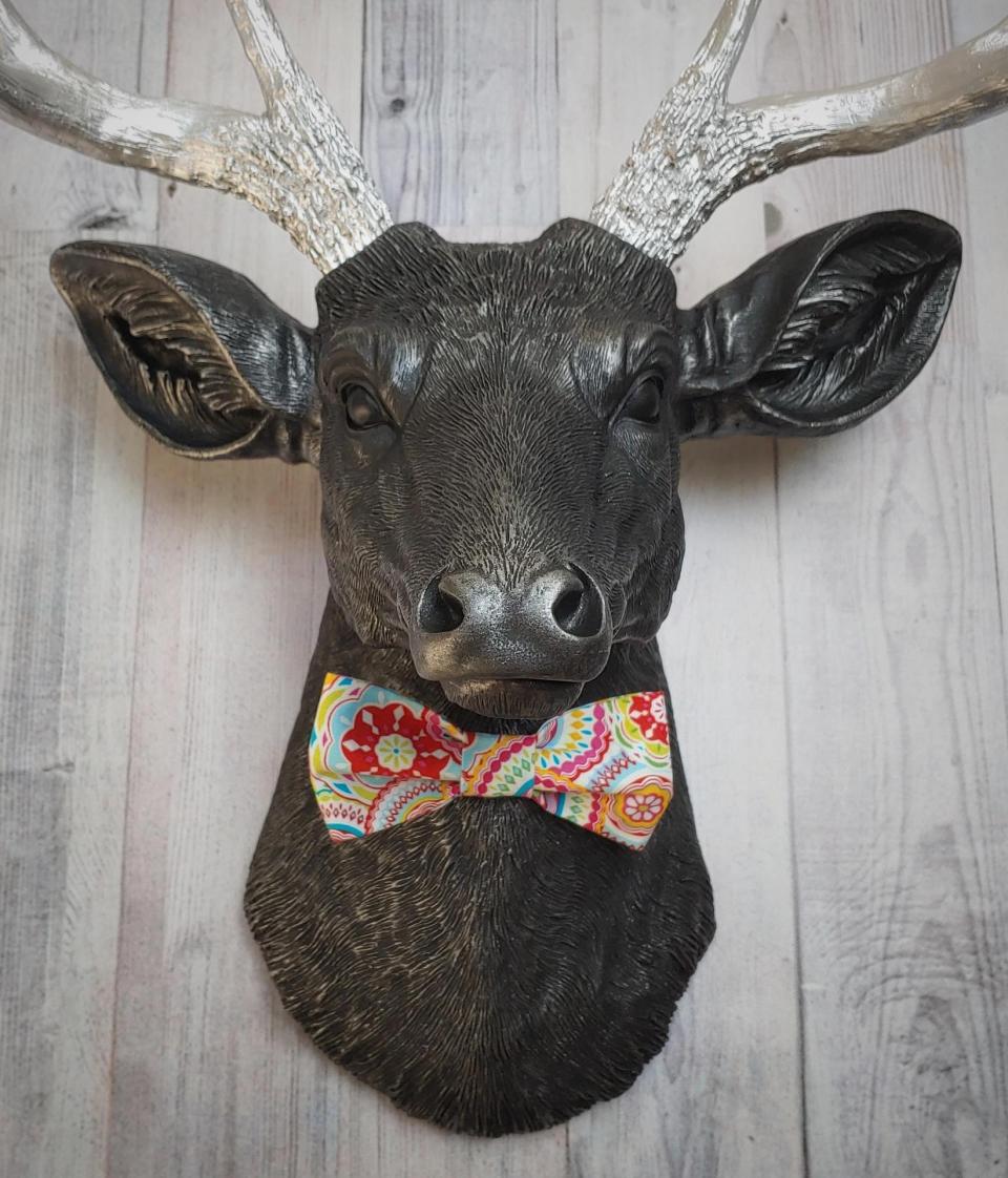 Faux taxidermy deer head painted black with silver antlers and a removable bright multi colored bow tie
