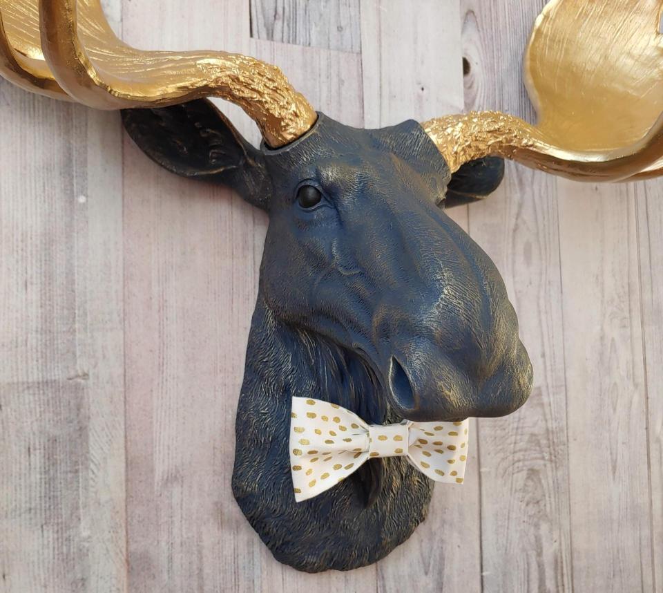Faux taxidermy moose head painted midnight blue with metallic gold antlers. A white and gold polka dot bow tie accents the neck of the moose.
