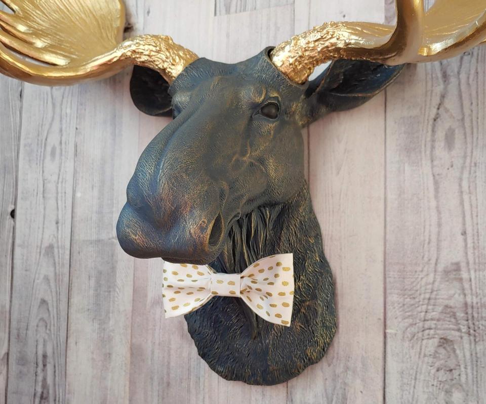 Faux taxidermy moose head painted midnight blue with metallic gold antlers. A white and gold polka dot bow tie accents the neck of the moose.