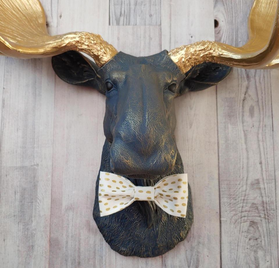 Faux taxidermy moose head painted midnight blue with metallic gold antlers. A white and gold polka dot bow tie accents the neck of the moose.