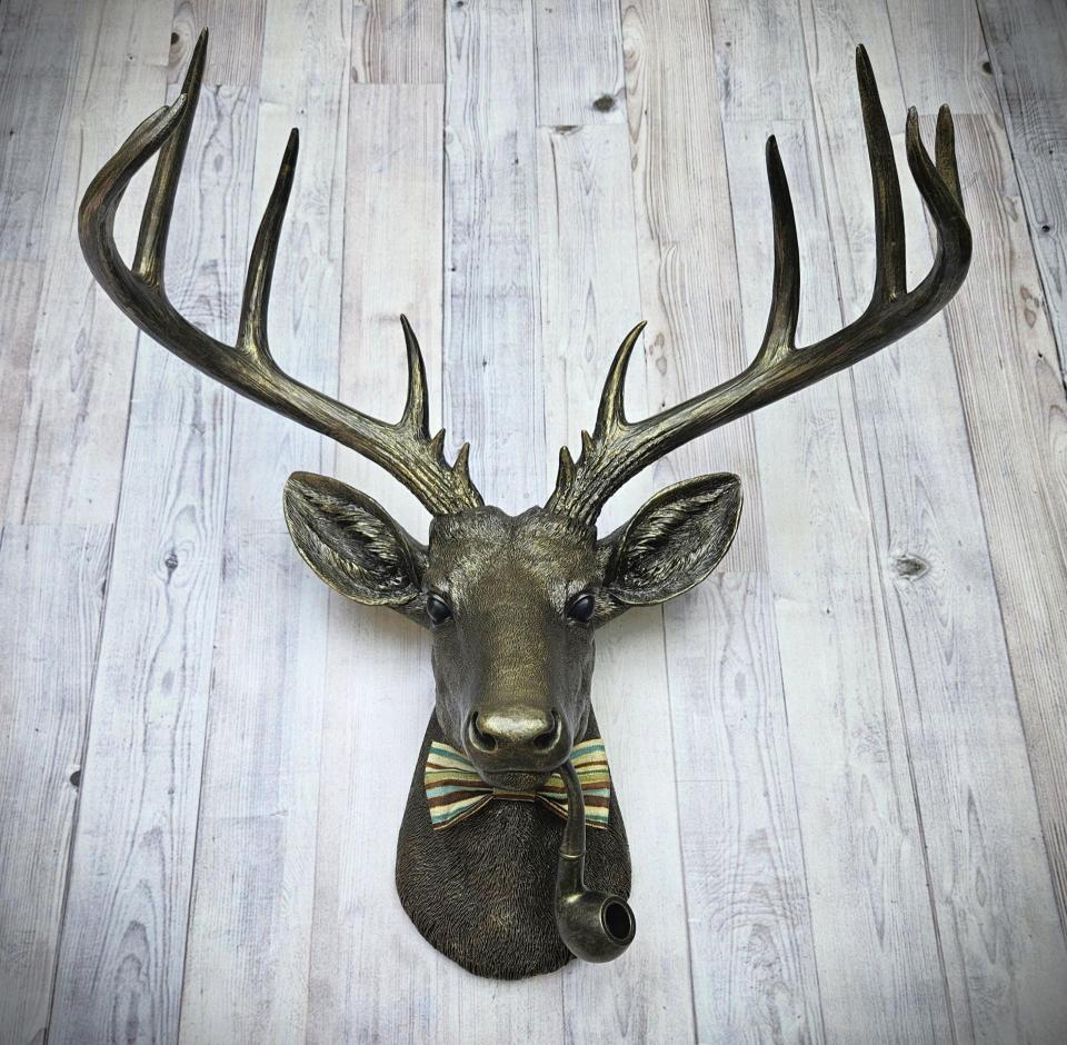 faux taxidermy deer head, rubbed bronze with gold accents. A smoking pipe hangs from the deers mouth and its wearing a striped bow tie