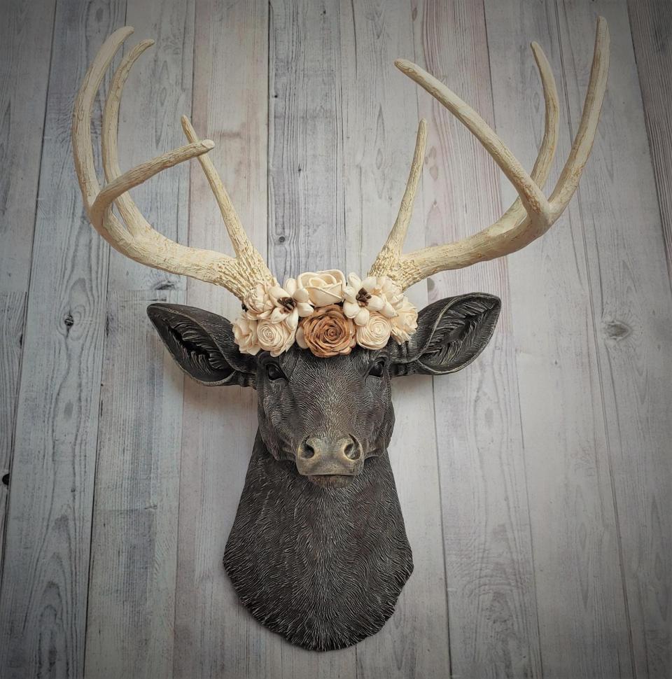 Faux taxidermy deer head, painted chestnut brown with antique white and gold accenting. Antlers are antique white with gold and chestnut brown accenting. A cream floral crown rests atop the deers head.