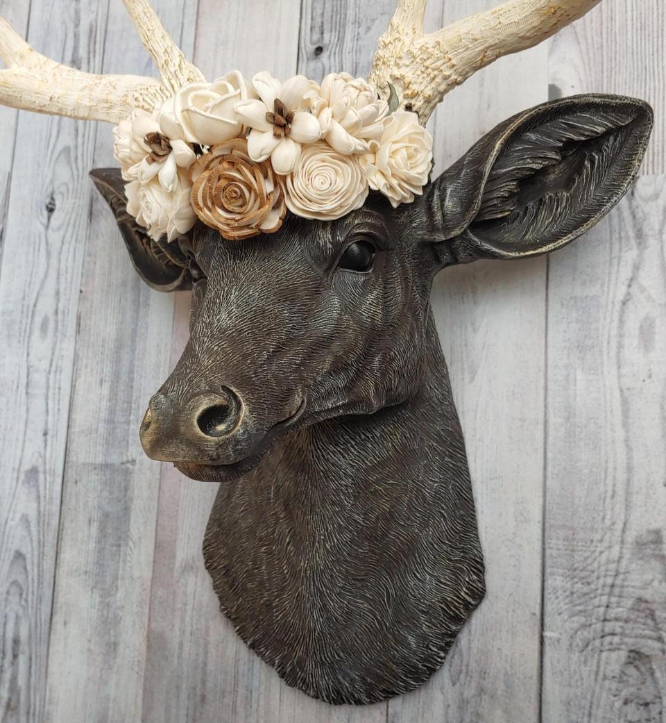 Faux taxidermy deer head, painted chestnut brown with antique white and gold accenting. Antlers are antique white with gold and chestnut brown accenting. A cream floral crown rests atop the deers head.