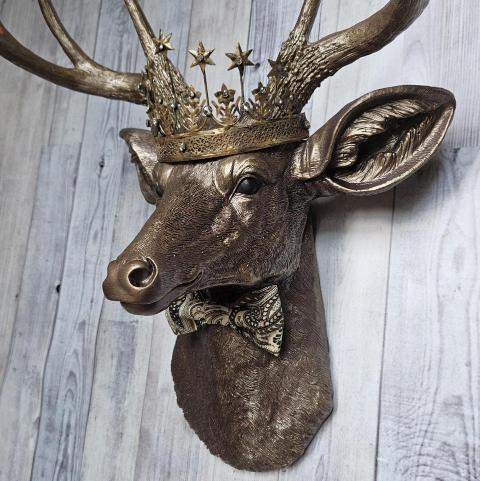 Faux taxidermy deer head wall mount with crown and bow tie.
